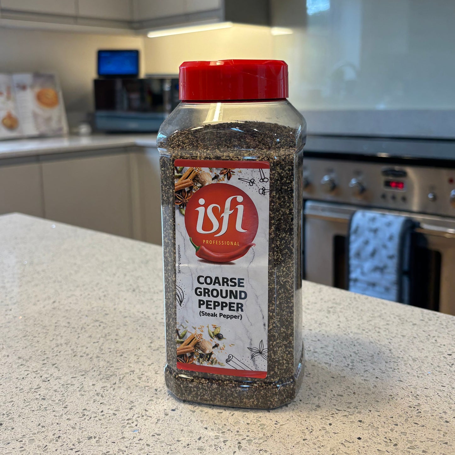 Bottle of Isfi course ground black pepper on a kitchen counter with appliances in the background
